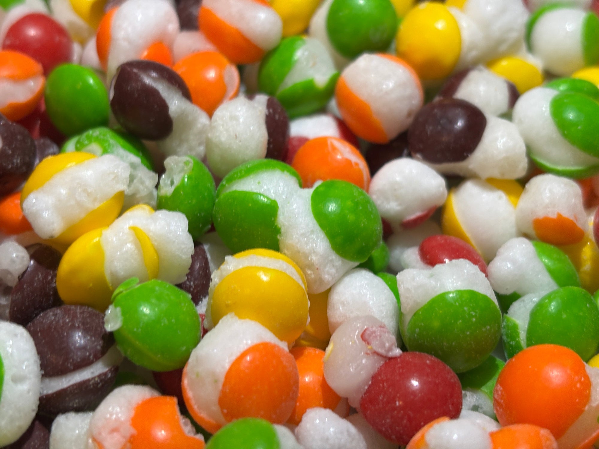 Assorted closeup view of freeze-dried skittles candies colors: red, green, orange, and white.