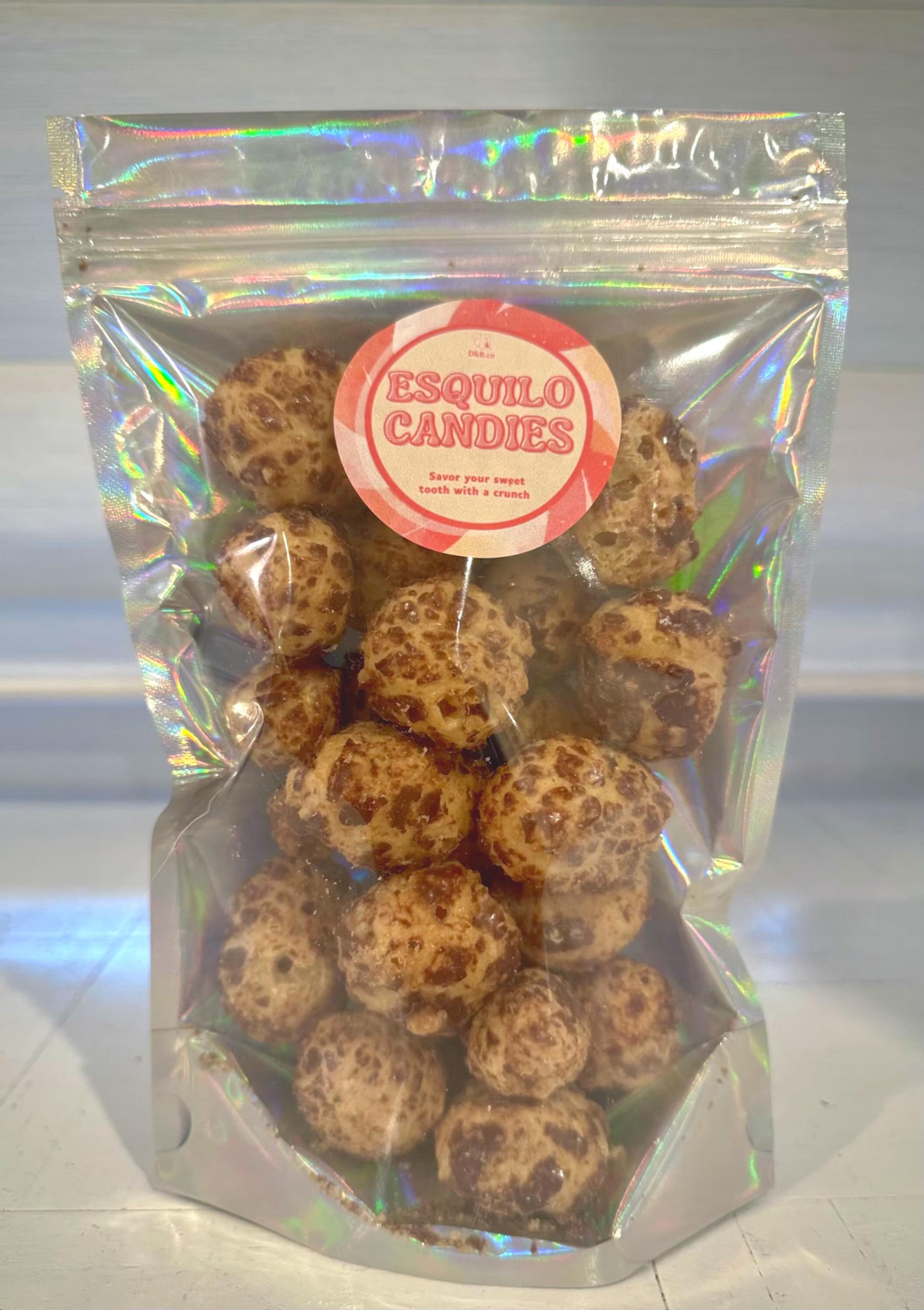 Clear bag with truffle-shaped chocolate caramel candies and 'Esquilo Candies' label on a reflective surface.