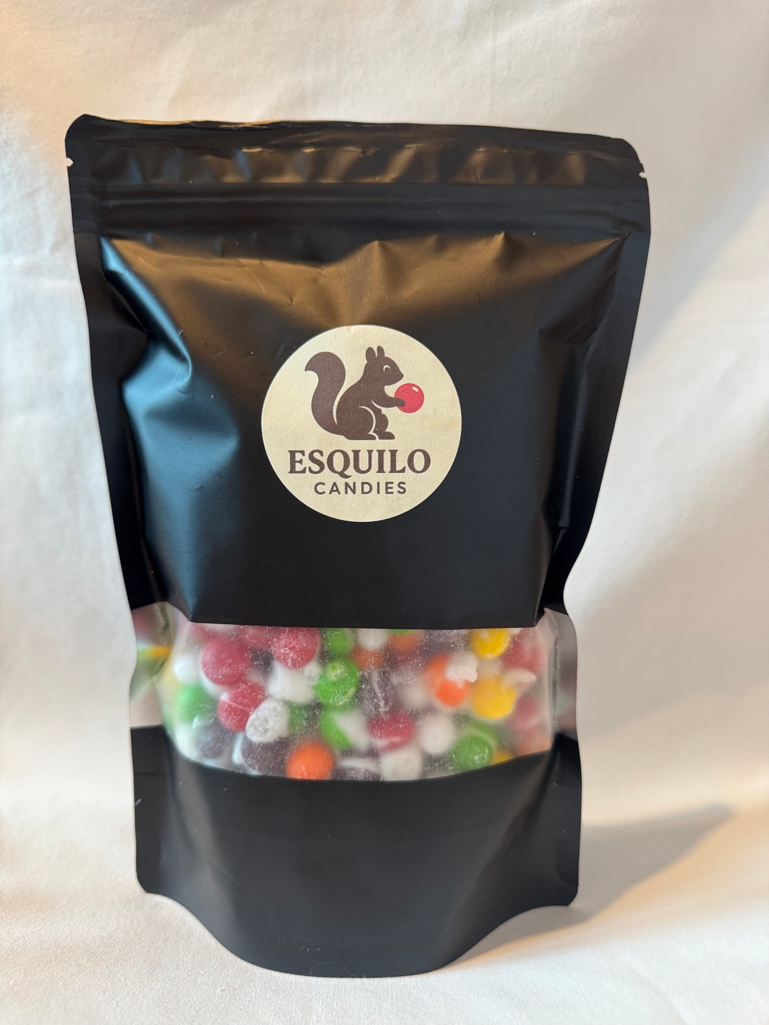 Black bag of Esquilo candies with a clear window showing freeze dried skittles on a white background